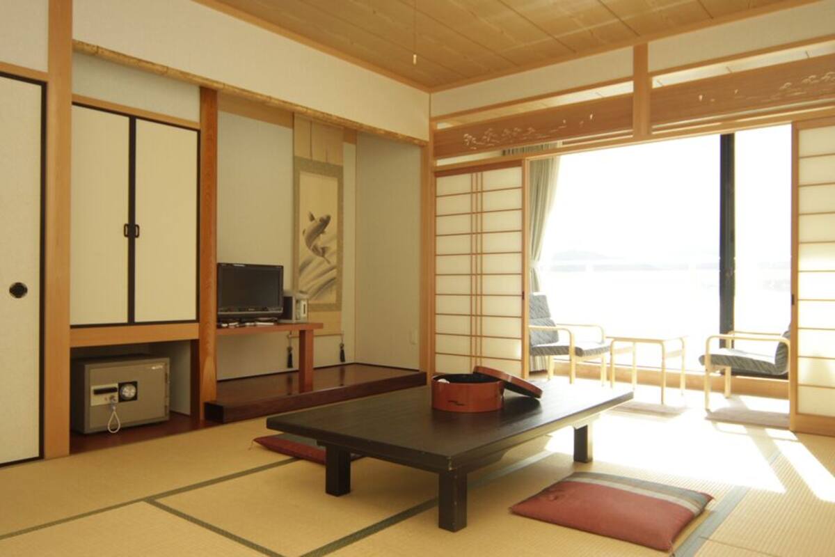 A traditional Japanese room with tatami flooring, a low table, a television, sliding doors, and a view through a window.
