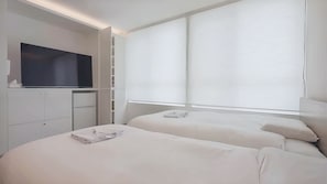 Una habitación de hotel moderna con dos camas, un televisor, un armario y una ventana con persianas.