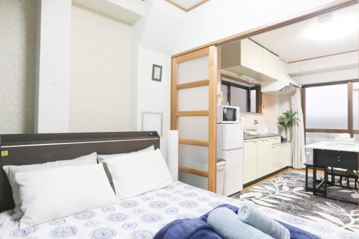 A hotel room with a bed, a small kitchenette, a dining area, and a sliding door leading to another room.