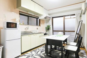 A compact kitchen with a microwave, sink, and cabinets. There's a dining table with chairs and a plant. - Comodita Takeyacho 1f (Kyoto)