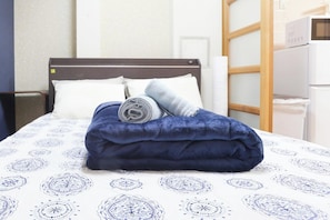 A neatly made bed with a dark blue blanket and rolled towels, white pillows, and a patterned bedspread. - Comodita Takeyacho 1f (Kyoto)