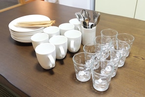 A table with white plates, cups, and a container holding utensils. - Comodita Takeyacho 1f (Kyoto)