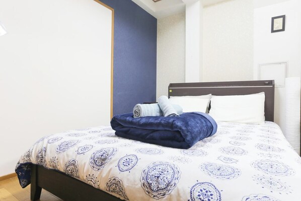 A neatly made bed with a patterned bedspread, a dark blue throw blanket, and two rolled towels. - Comodita Takeyacho 1f (Kyoto)