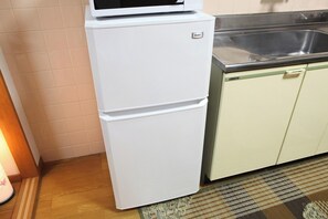 A white refrigerator with a microwave on top, located in a kitchen with light-colored cabinets and a stainless steel sink. - Comodita Takeyacho 1f (Kyoto)