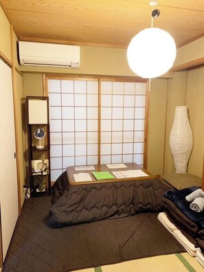 A traditional Japanese-style room with tatami flooring, a low table with papers, a shoji screen door, and a hanging light fixture. - Comodita Takeyacho 1f (Kyoto)