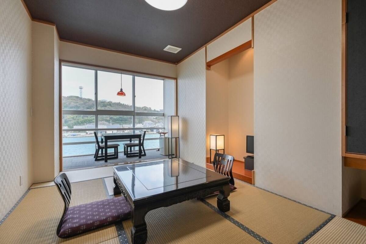 A traditional Japanese-style room with tatami flooring, a low table, and a view of the sea.