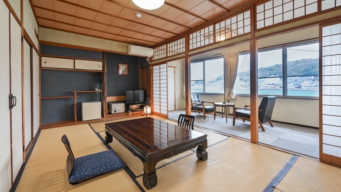 Ein traditioneller japanischer Raum mit Tatami-Böden, einem niedrigen Tisch und Schiebetüren, die auf einen Balkon mit Aussicht führen.