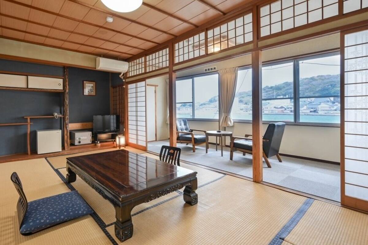 A traditional Japanese room with tatami flooring, a low table, and sliding doors leading to a balcony with a view.