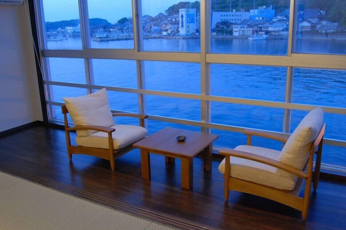 A room with a large window overlooking a body of water, two wooden chairs, a small table, and a tiled floor.