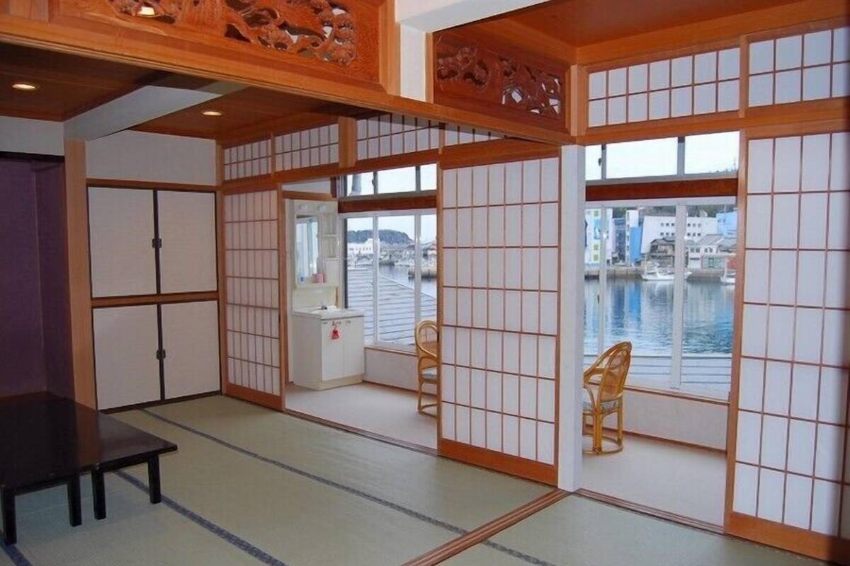 A traditional Japanese room with tatami flooring, shoji screens, and a view of a water body.