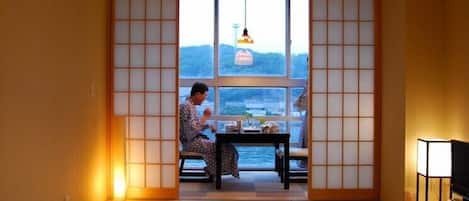 A traditional Japanese room with tatami flooring, a low table, and a view of the sea through shoji screens.