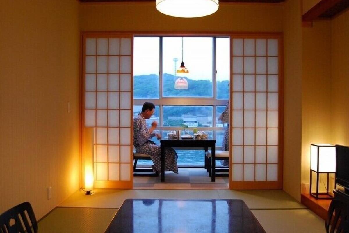 A traditional Japanese room with tatami flooring, a low table, and a view of the sea through shoji screens.