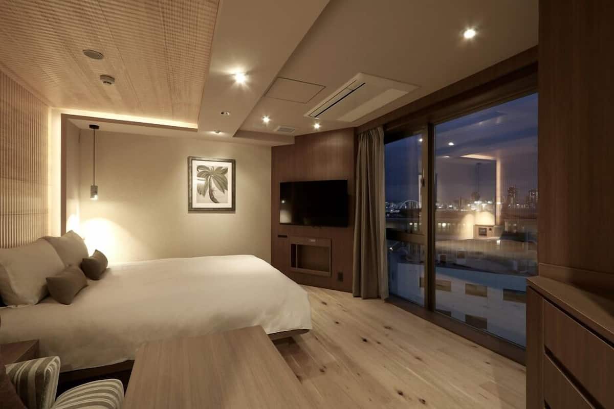 Ett modernt hotellrum med en stor säng, en platt-TV, ett stort fönster med utsikt över staden och ett tak med infälld belysning.