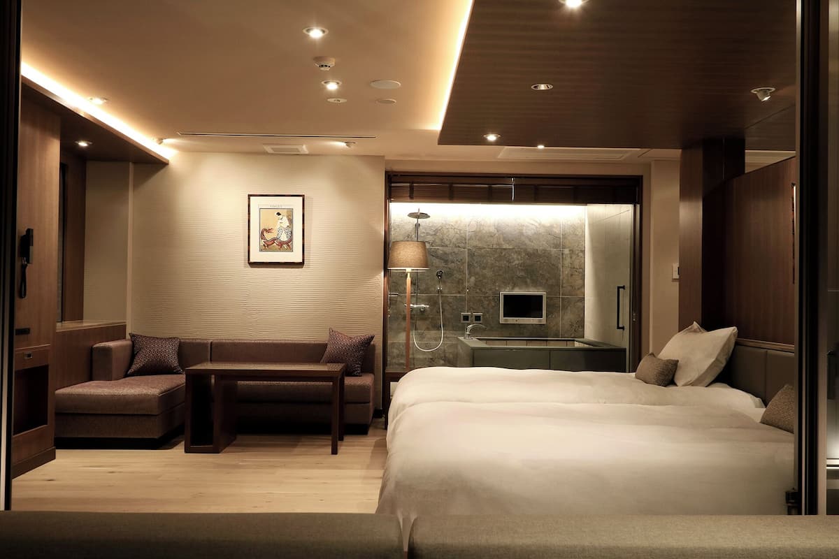 Ett modernt hotellrum med en stor säng, en sittgrupp med ett bord, en dusch och en väggmonterad TV.