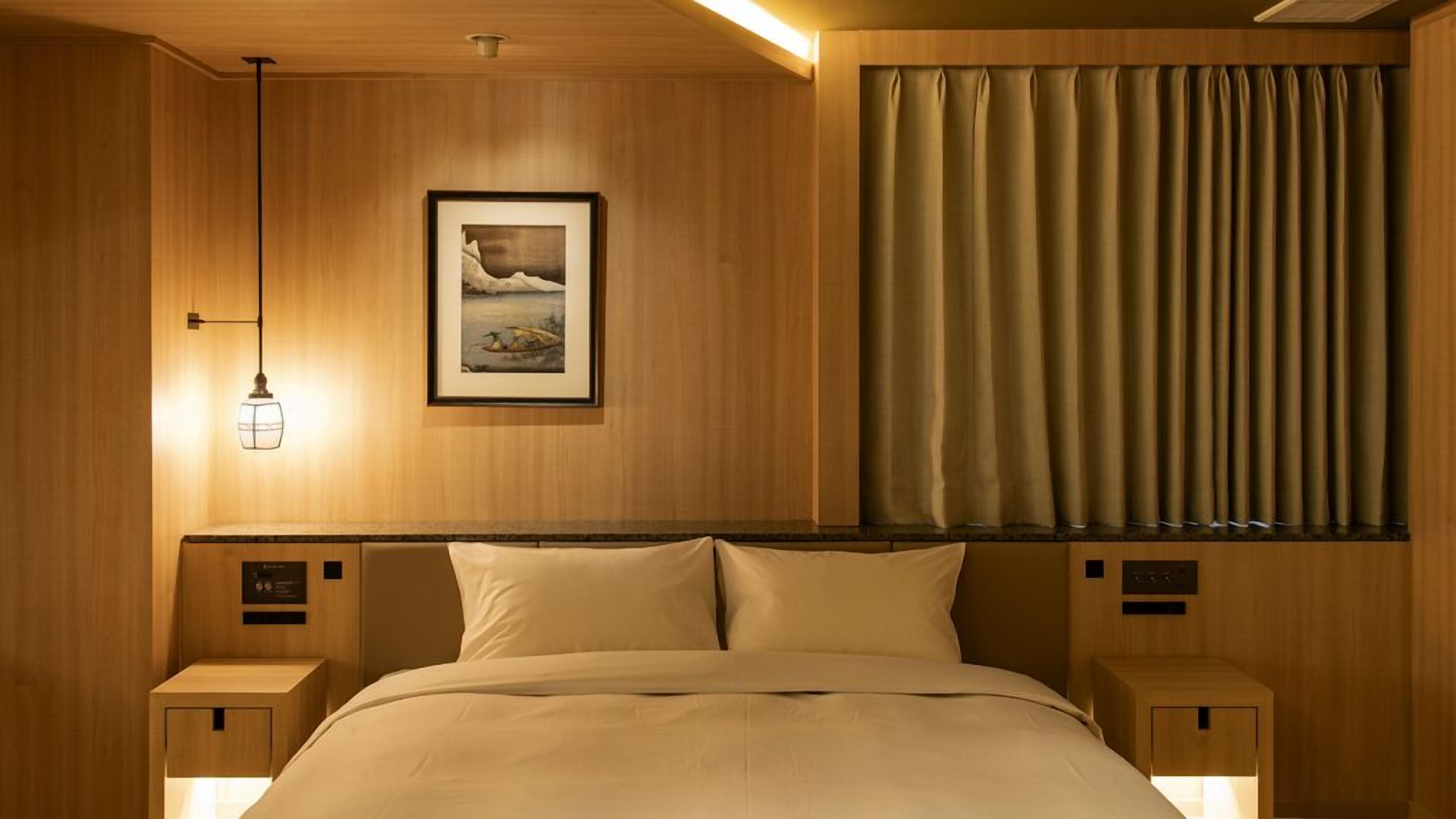 A hotel room with a wooden headboard, a framed picture, a bed with white linens, and a window with curtains.