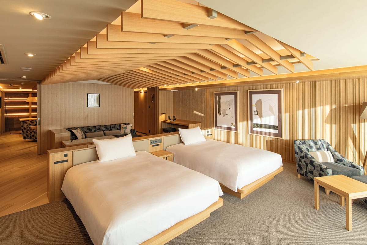 Ett modernt hotellrum med två sängar, en soffa, ett skrivbord och en stol.