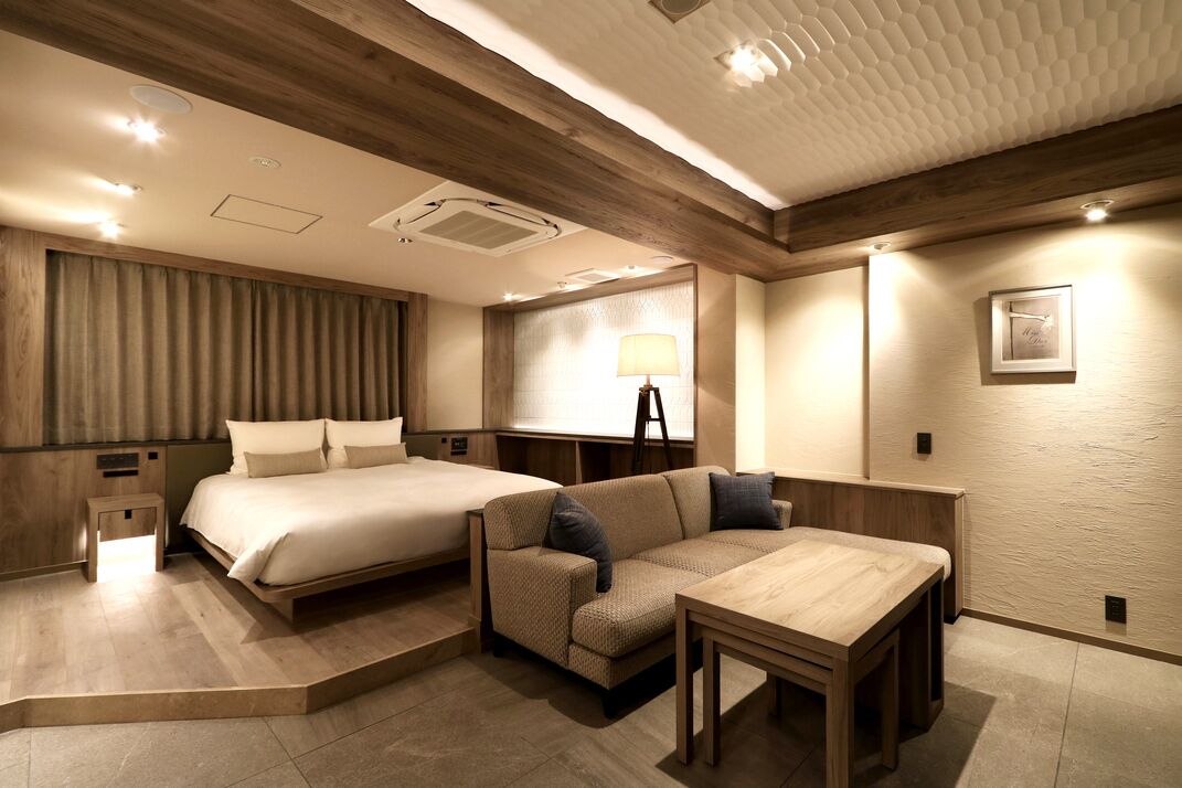 A hotel room with a bed, sofa, table, and lamp.