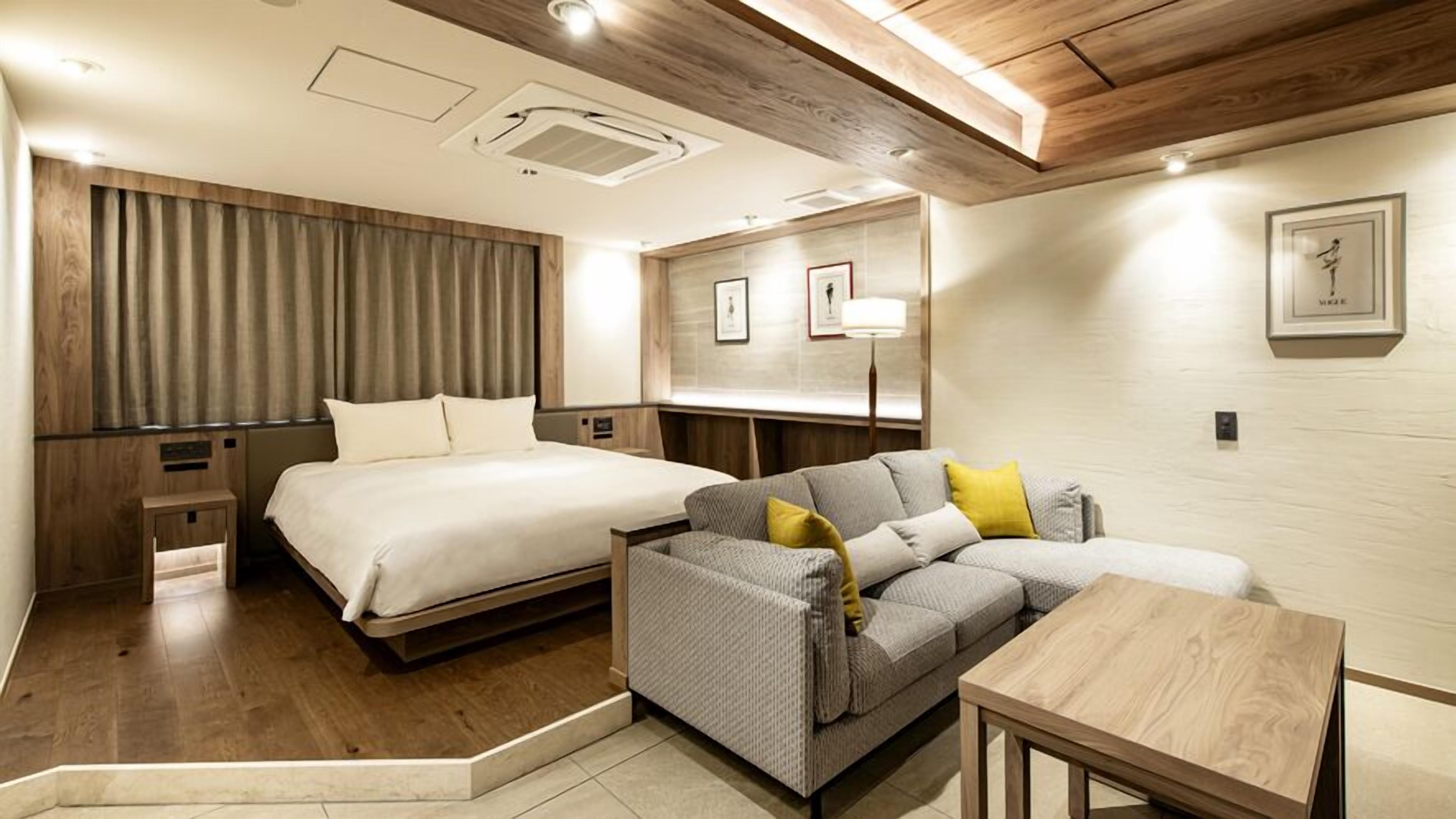 A hotel room with a bed, a sofa, a small table, and a mirror.