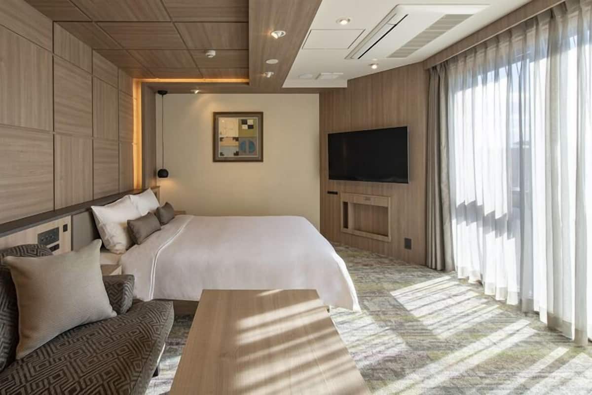Ett hotellrum med en stor säng, en soffa, en tv och ett stort fönster med gardiner.