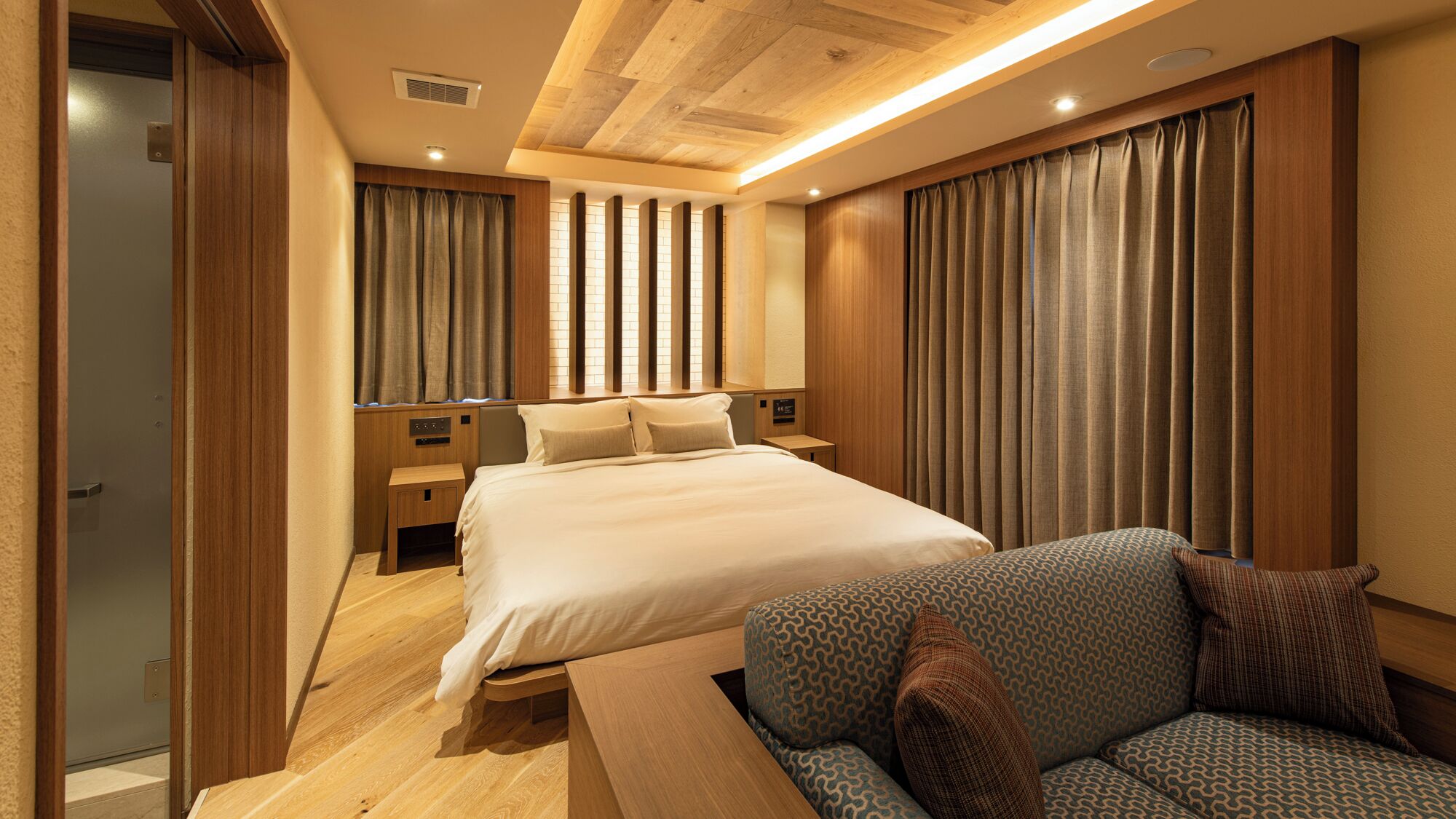A hotel room with a large bed, a sofa, wooden flooring, and a ceiling with wooden beams.