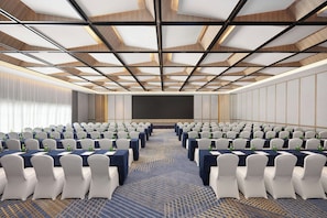 A conference room with rows of tables and chairs, a large screen, and a patterned carpet.