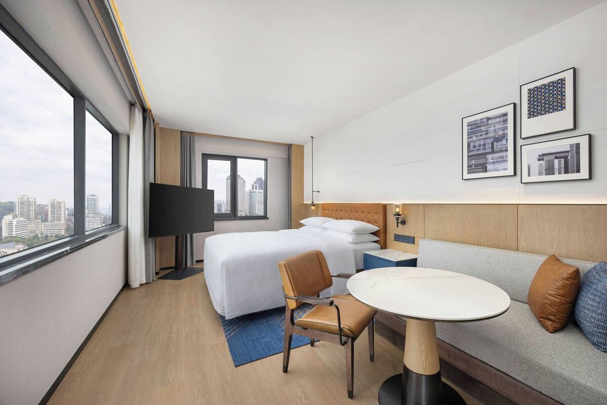 A hotel room with a bed, a sofa, a table, and a TV.