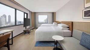 Una camera d'albergo con una grande finestra, un letto, un divano, una scrivania e una televisione.