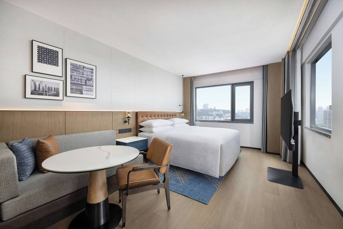 A hotel room with a bed, a sofa, a dining table, a chair, a TV, and framed pictures on the wall.