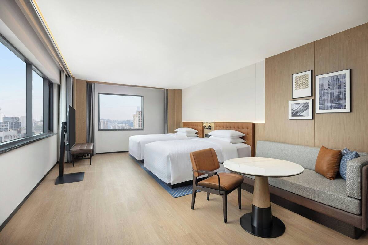 A hotel room with two beds, a sofa, a dining table, and a view of the city.