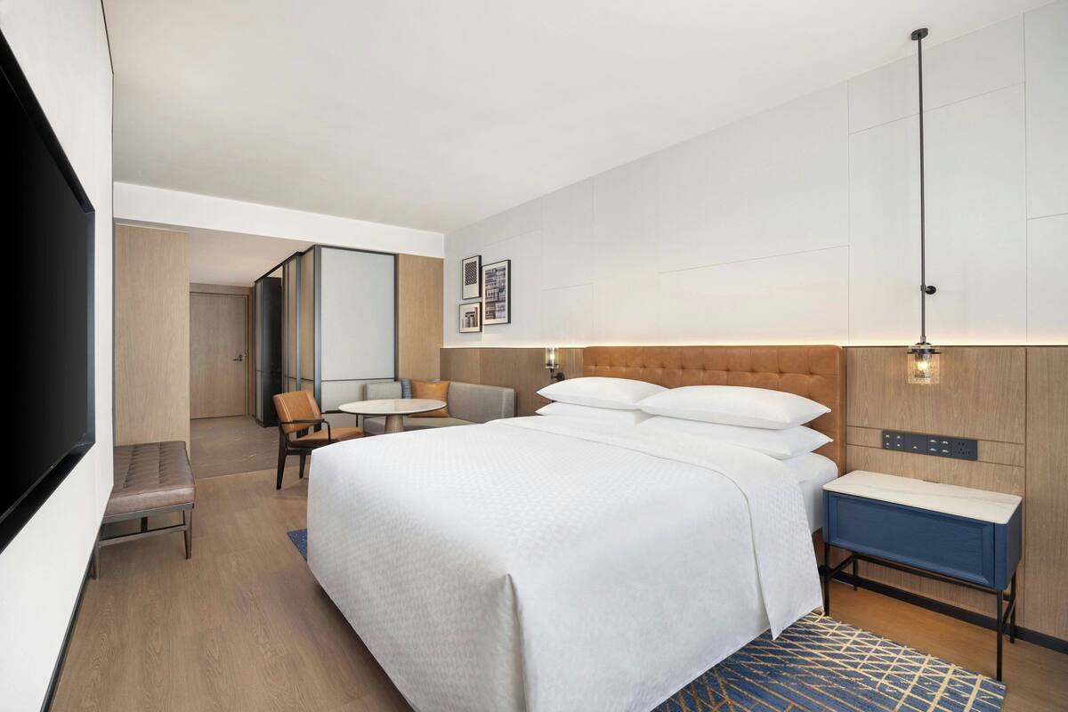 A modern hotel room with a large bed, a desk, a chair, and a television.