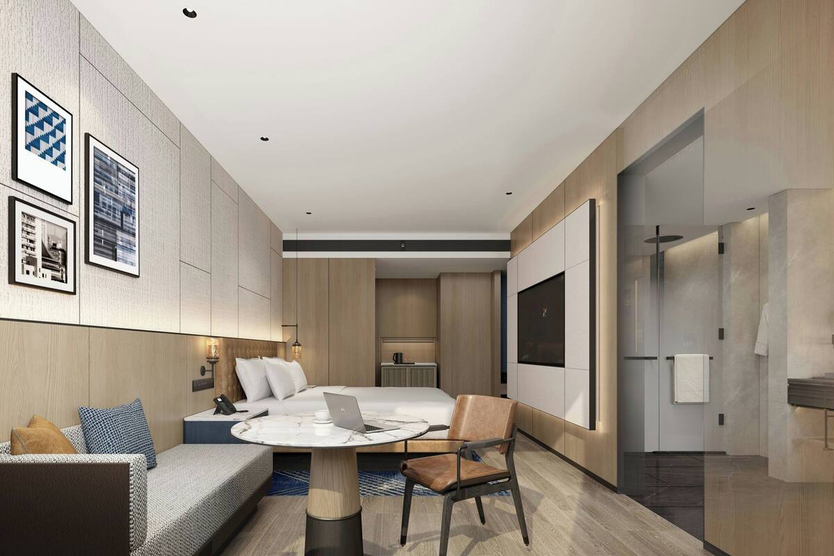 A modern hotel room with a bed, a desk with a laptop, a chair, a sofa, and a TV.