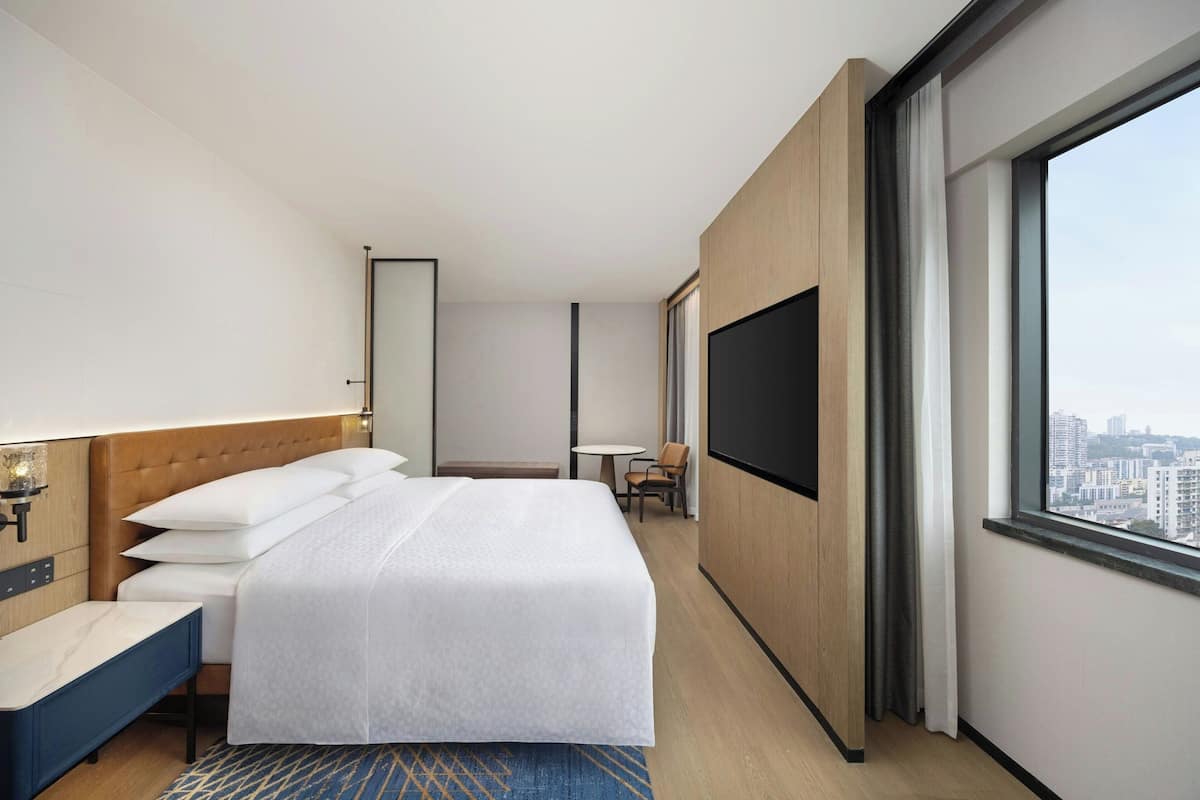 A hotel room with a bed, bedside table, TV, and a city view.