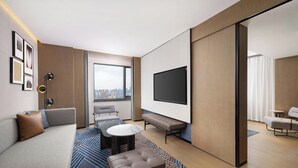 Camera d'albergo moderna con divano, tavolino rotondo, panca, televisore e vista sulla città.