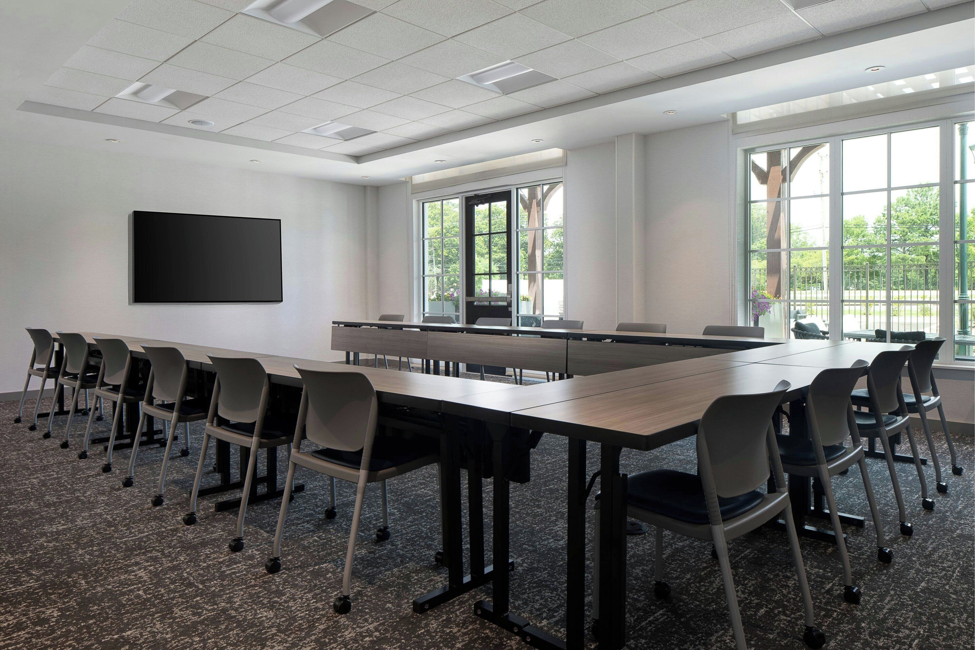 A conference room with a long table, chairs, a flat-screen TV, and large windows.