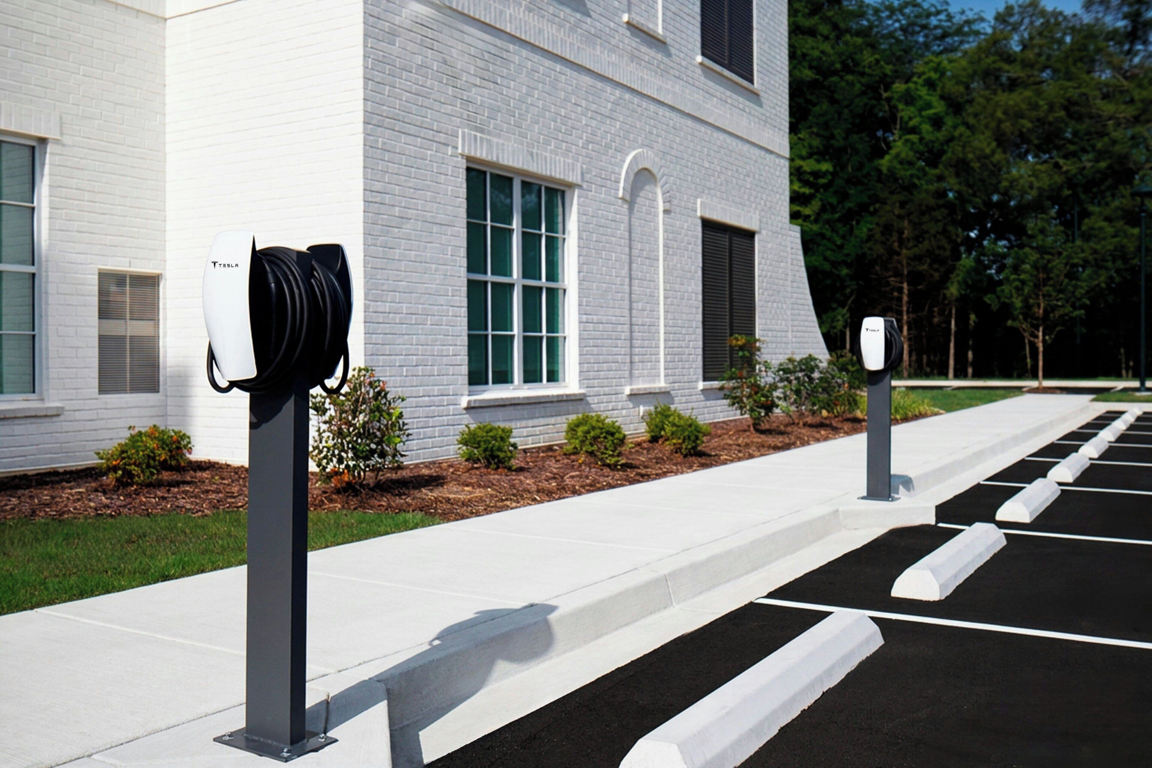 A parking area with electric vehicle charging stations in front of a building with white brick walls and windows.