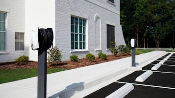 A parking area with electric vehicle charging stations in front of a building with white brick walls and windows.