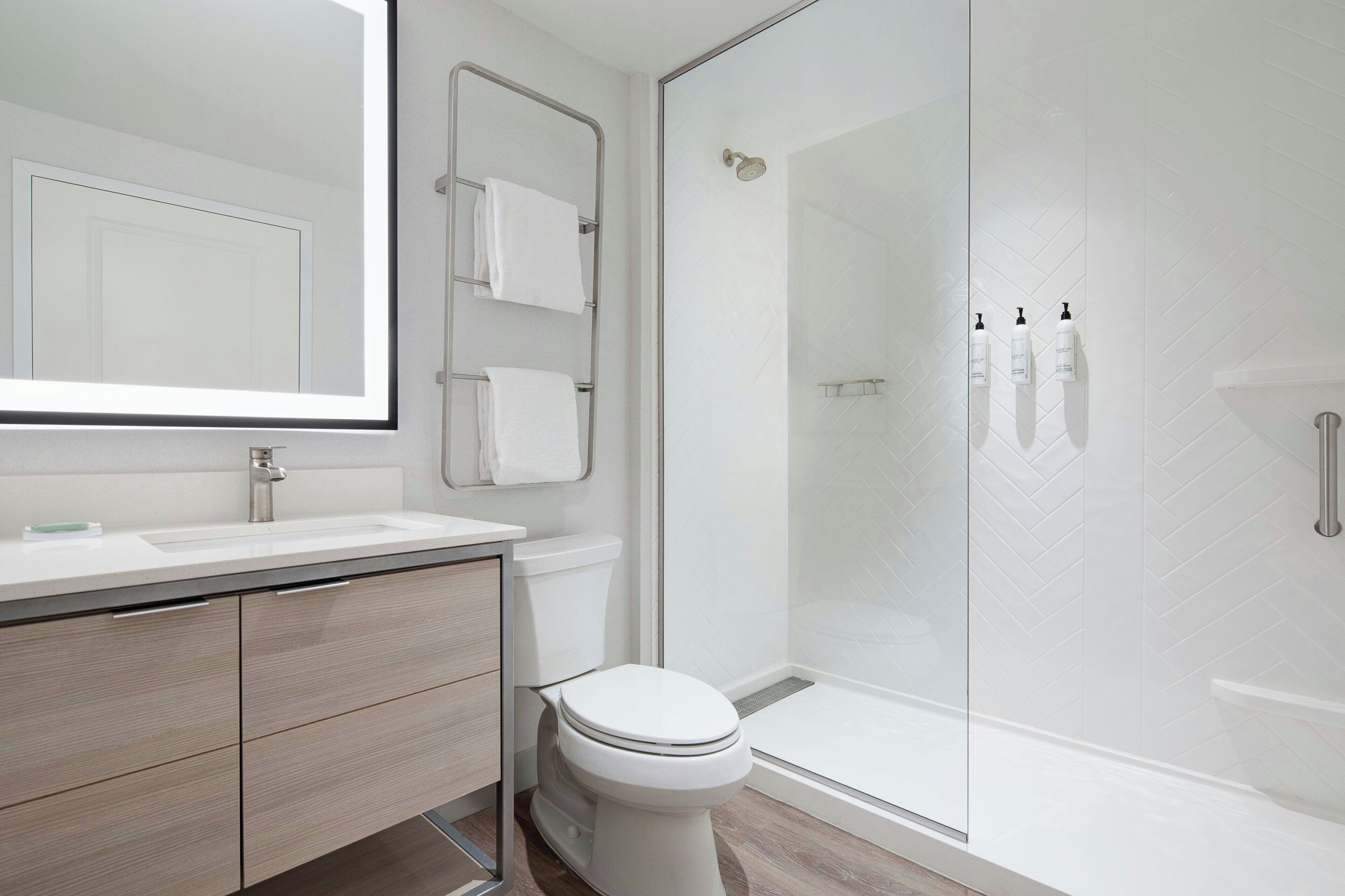 A modern bathroom with a glass-enclosed shower, a toilet, a vanity with a mirror, and a towel rack.