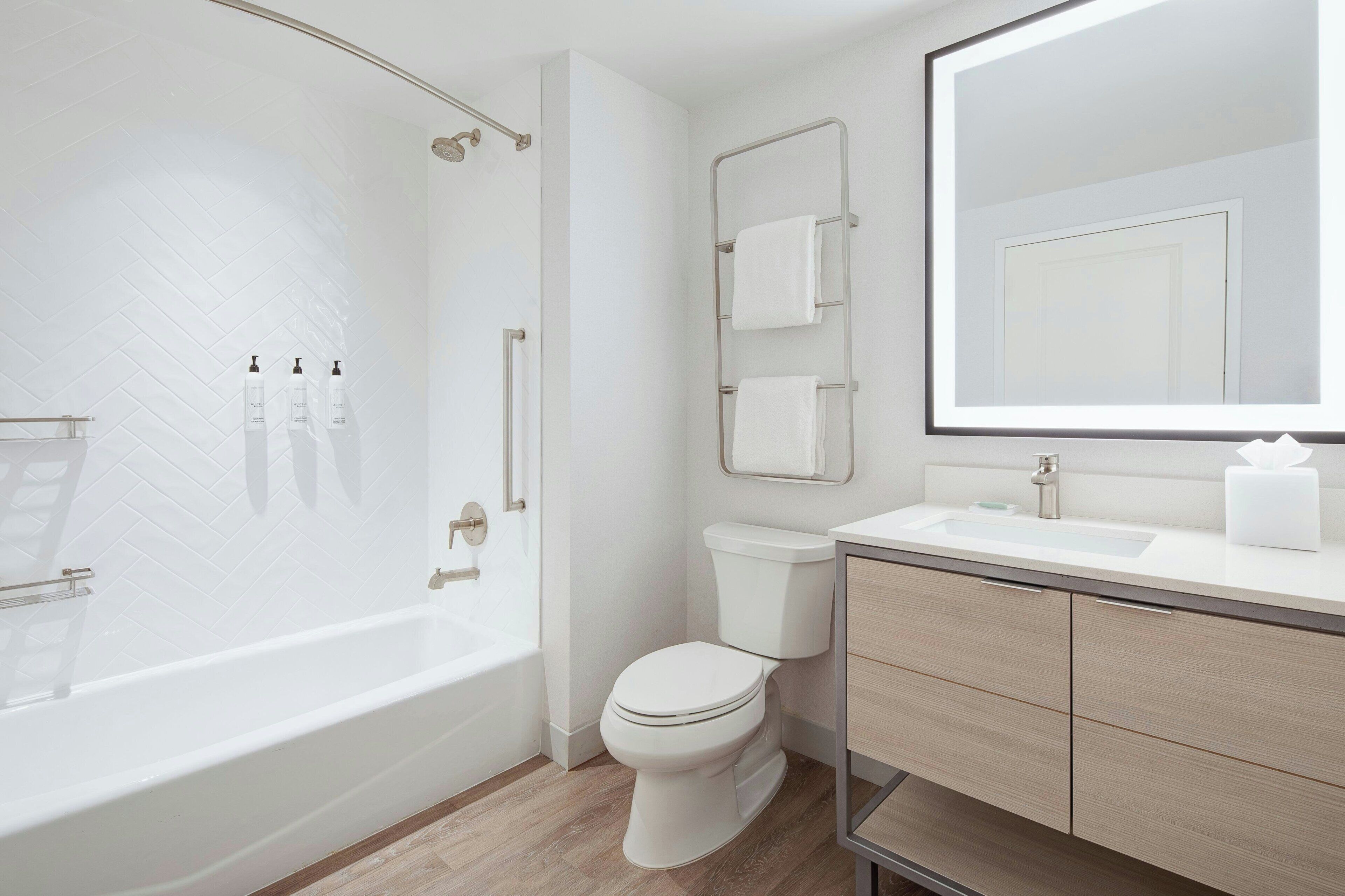 A modern bathroom with a freestanding bathtub, a toilet, a vanity with a mirror, and a towel rack.