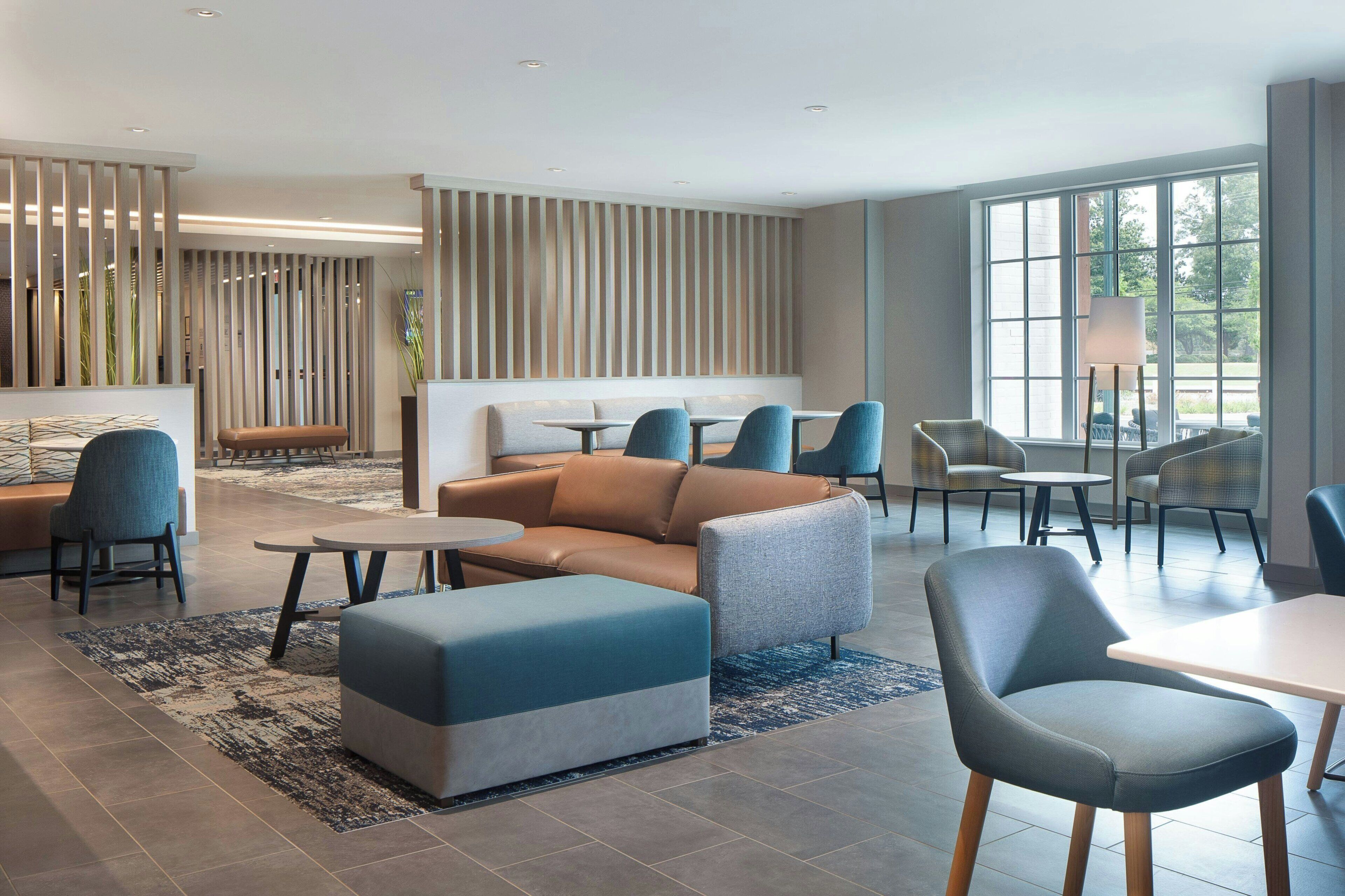 Un hall d’hôtel moderne, doté d’espaces aménagés avec des sièges, d’un comptoir d’accueil et de grandes fenêtres laissant entrer la lumière naturelle.