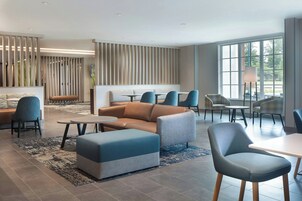 Un moderno vestíbulo de hotel con zonas de estar, un mostrador de recepción y grandes ventanales que dejan entrar luz natural.