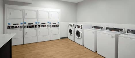 A laundry facility with multiple washing machines and dryers, a wooden floor, and a white wall.