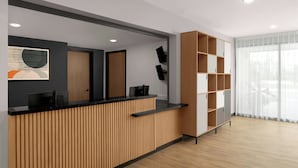 A reception desk with a wooden finish, a black countertop, and a modern design. There is a large window with sheer curtains, and a wooden shelving unit to the right. - StudioRes by Marriott Mesa (Mesa)