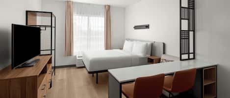 A modern hotel room with a bed, desk, chairs, a TV, and a window with curtains.