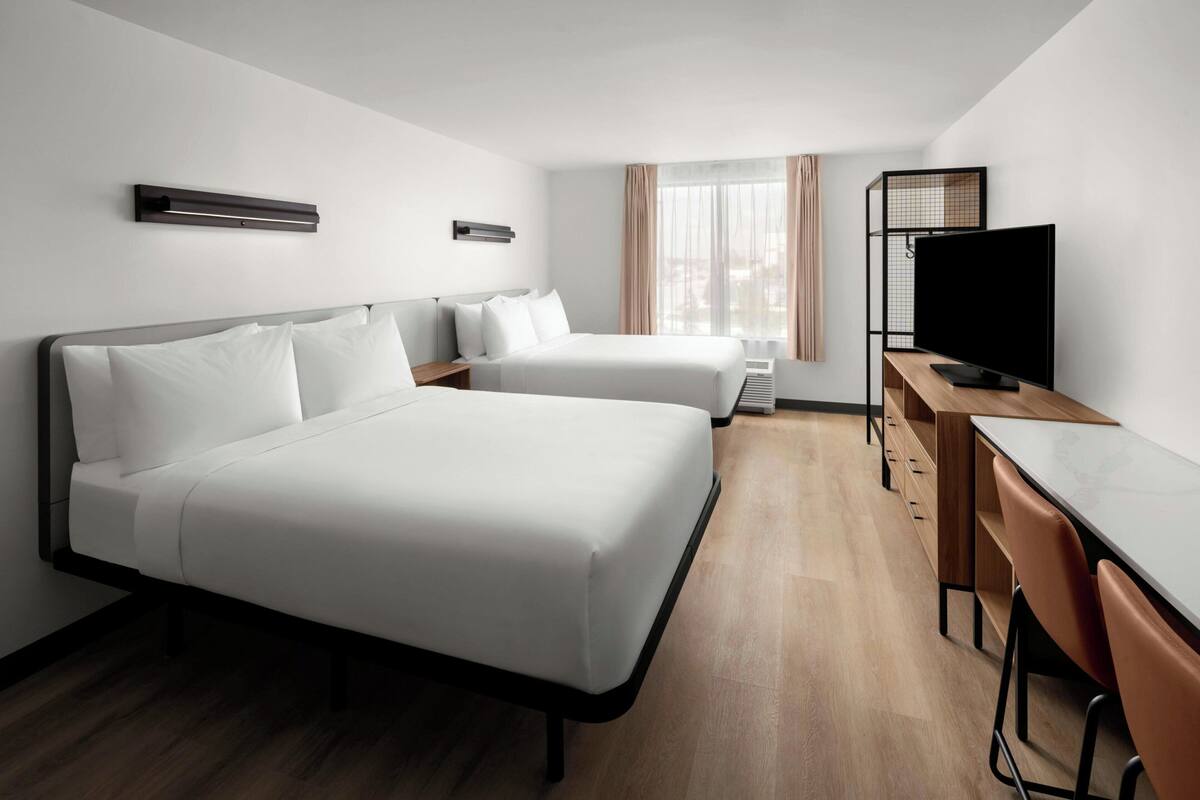 Habitación de hotel con dos camas, un escritorio, un televisor y una ventana con cortinas.