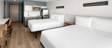A hotel room with two beds, a desk, a chair, a microwave, and a small kitchenette.
