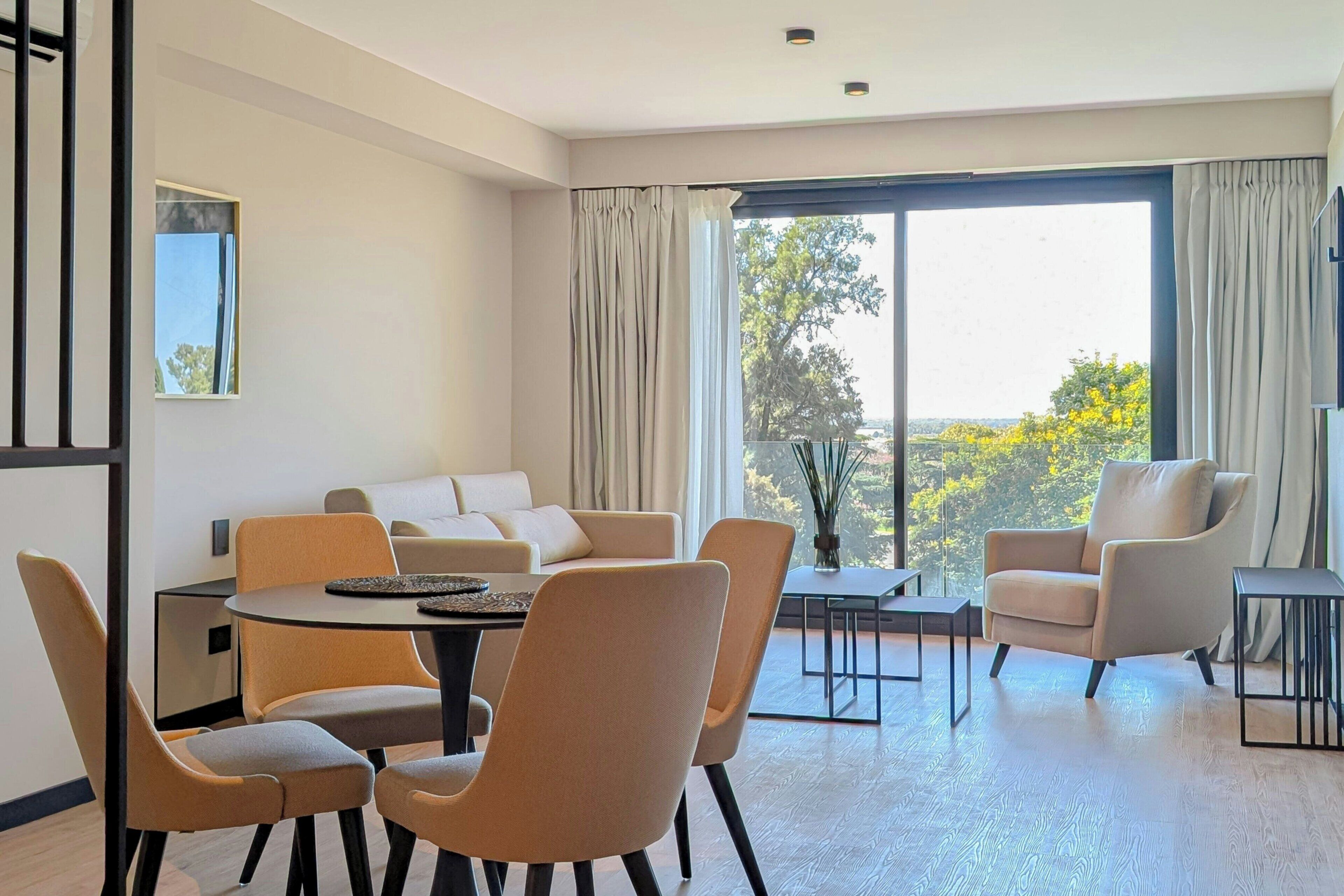 Una sala de estar moderna con sofá, mesa de comedor, sillas y un gran ventanal con cortinas.