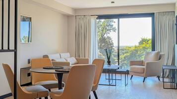 Una sala de estar moderna con sofá, mesa de comedor, sillas y un gran ventanal con cortinas.