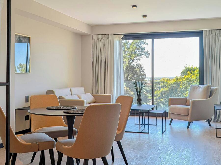 Una sala de estar moderna con sofá, mesa de comedor, sillas y un gran ventanal con cortinas.