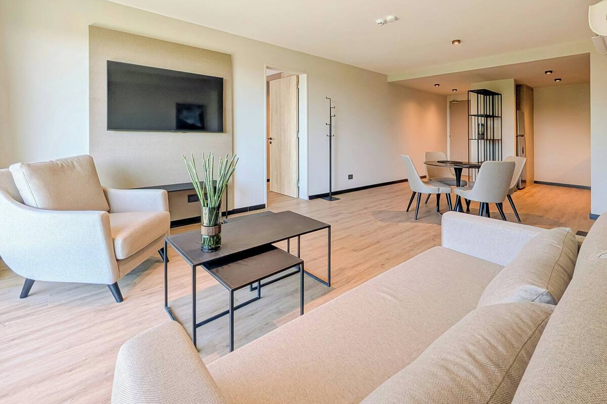 A modern living room with a sofa, armchair, coffee table, and a flat-screen TV mounted on the wall.