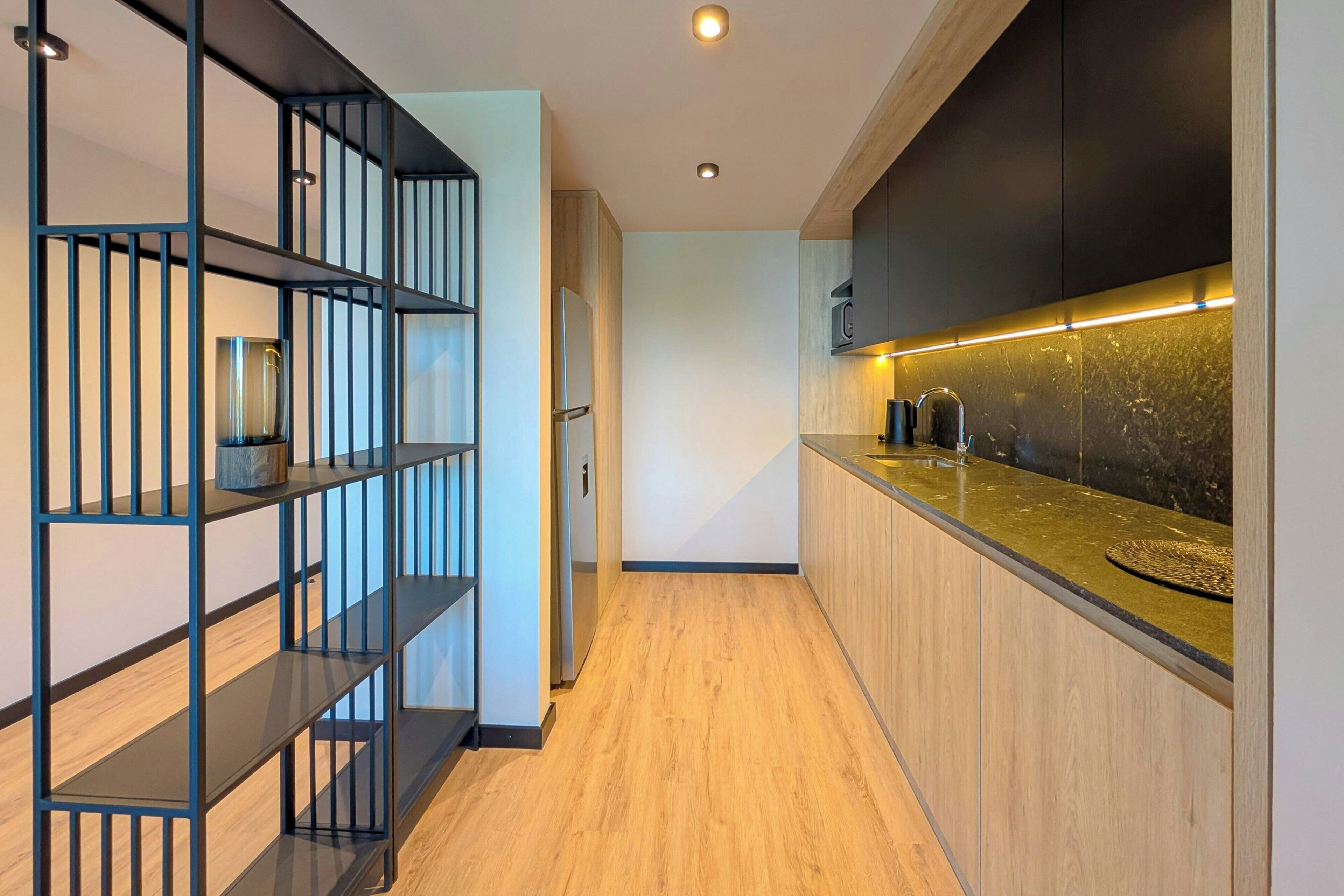 A modern kitchen with wooden flooring, black shelving, and a granite countertop.